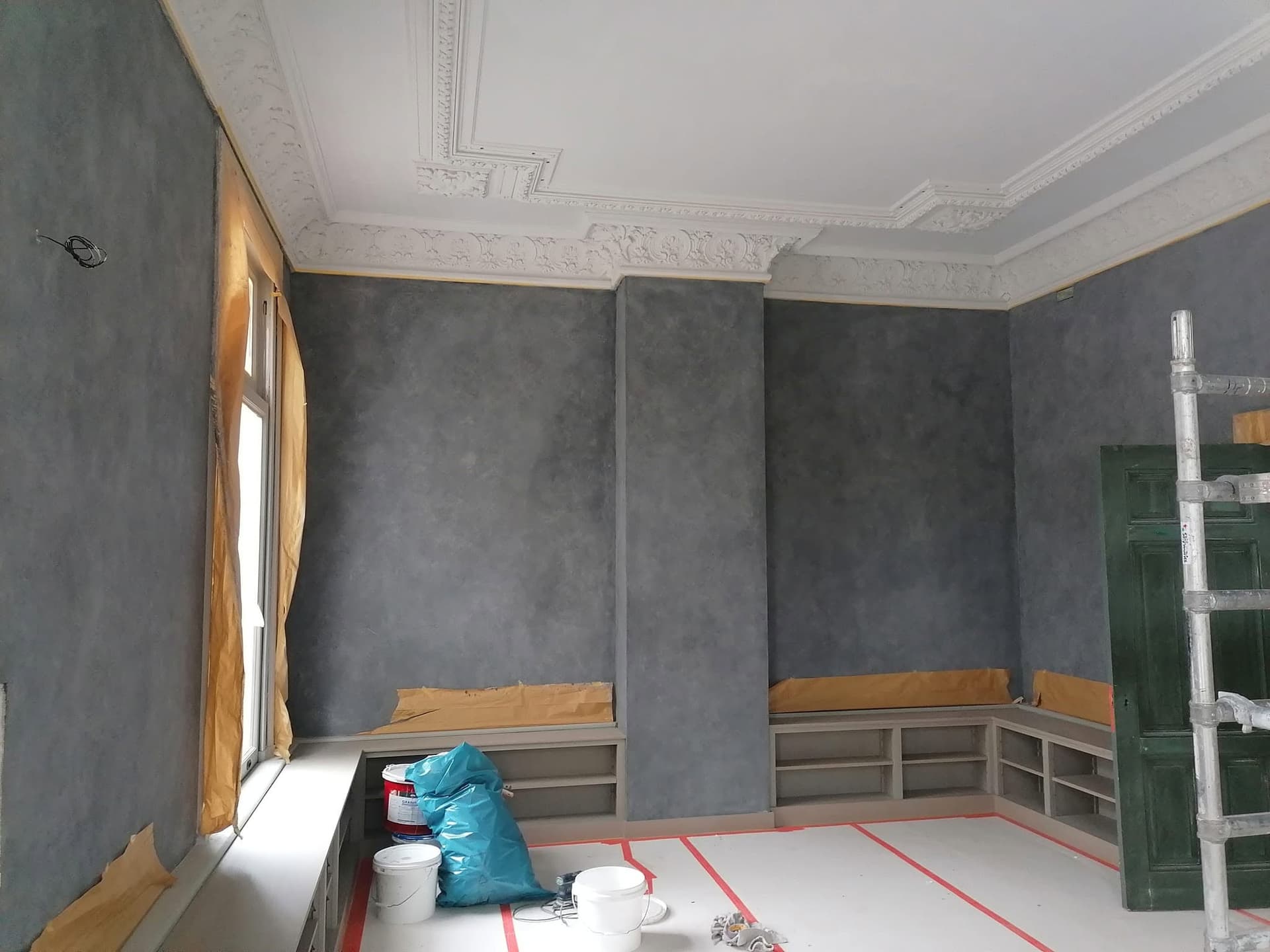 Salon met decoratieve grijze wandafwerking onder een sierlijk stucplafond