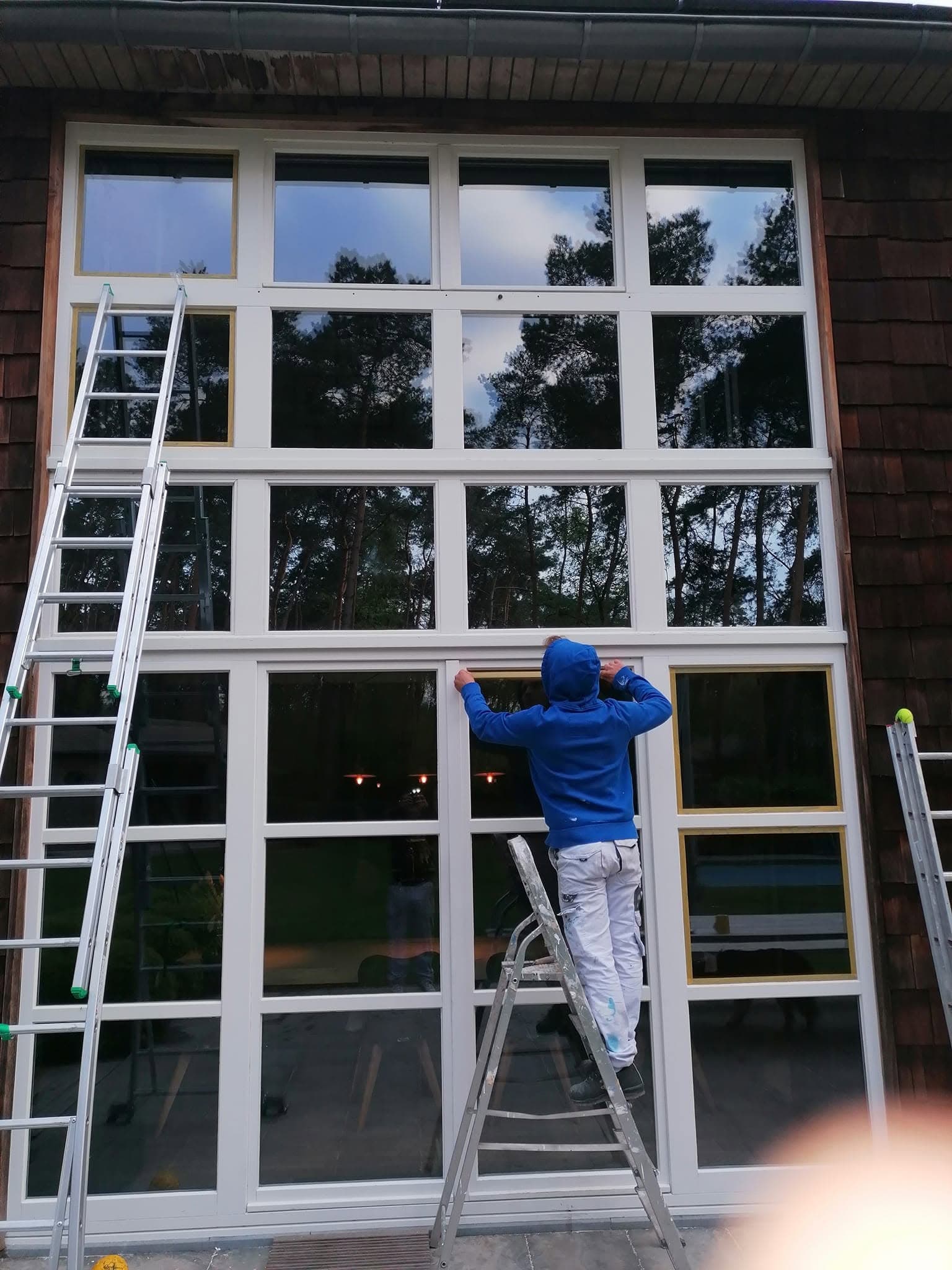 Schilder op een ladder werkt het witte buitenschrijnwerk van een hoge raampartij af